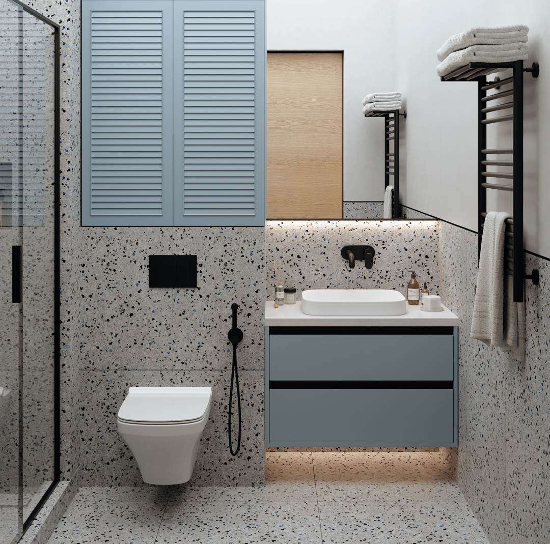 Ванная комната, выдержанная в дымчато-голубых тонах, словно окутана утренним туманом. Чёрная сантехника дерзко прочерчивает графичные линии, подчёркивая современный минимализм. Голубая мебель перекликается с серым терраццо на стенах, а дверь, отделанная шпоном натурального дуба, добавляет природной теплоты. Всё вместе создаёт ощущение гармонии, словно кусочек природы просочился в городскую квартиру. Натяжной потолок с мягкой подсветкой имитирует рассеянный дневной свет, добавляя уюта в эту минималистичную обитель. А зеркало во всю стену визуально стирает границы, превращая ванную в бесконечное, воздушное пространство.